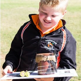 A young boy showing his science project, surrounded by nature.