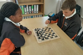 Two young school kids engaged in a chess game, focused intently at a table, showcasing their strategic thinking.