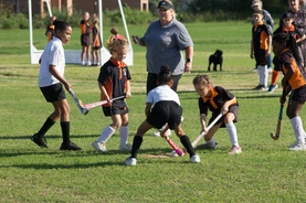 Children engaged in a lively game of field hockey, demonstrating teamwork and excitement on a sunny outdoor field.