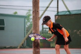 A young girl stands confidently, holding a tennis racket in one hand and a tennis ball in the other, ready to play.